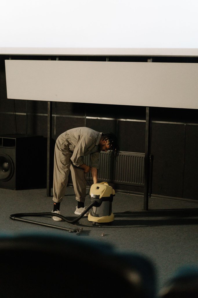 Worker in a jumpsuit vacuuming an auditorium carpet