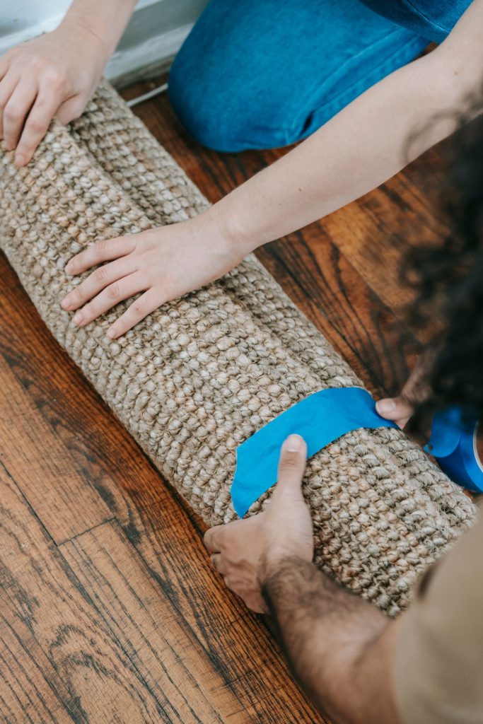 Two people holding a rolled carpet wrapped with blue tape