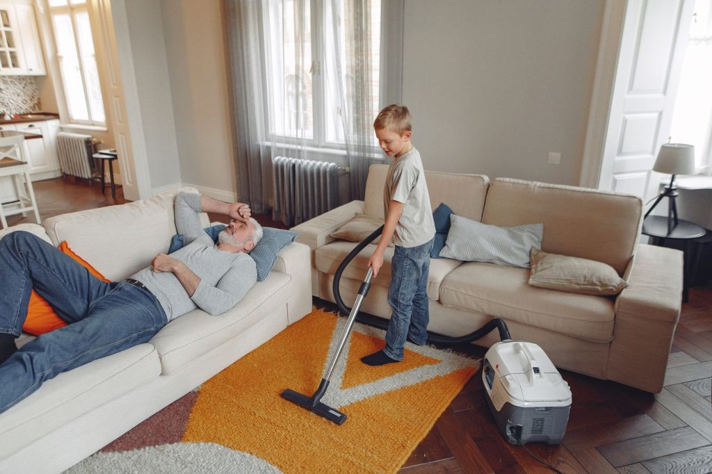 Family living room where a child vacuums the carpet beside a sofa