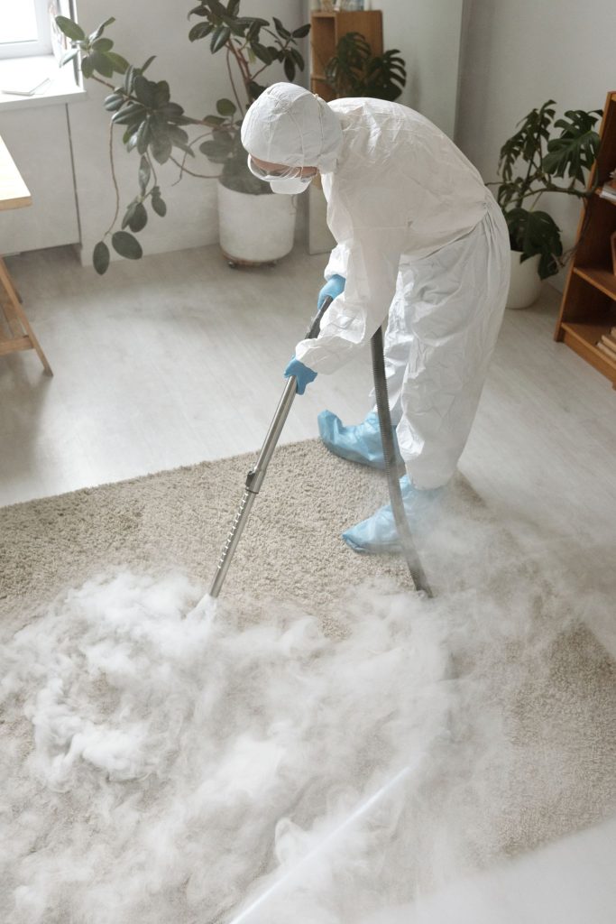 Person in protective gear spraying a sanitising treatment on a carpet